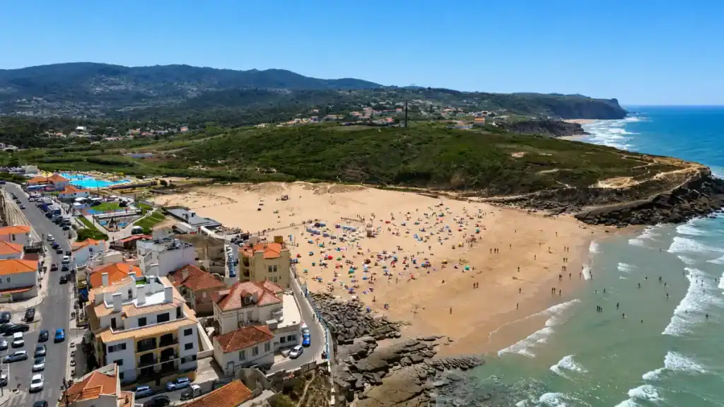 Aerial shot of Praia das Maçãs packed with sunbathers and swimmers beside a small coastal town
