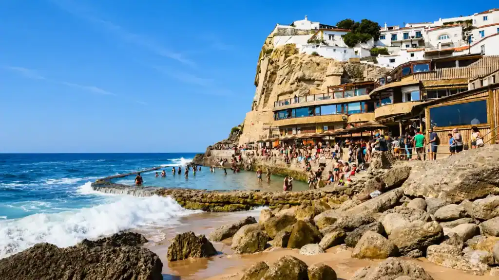 Crowds swimming in the tidal pool at Azenhas do Mar with a clifftop restaurant and white village above