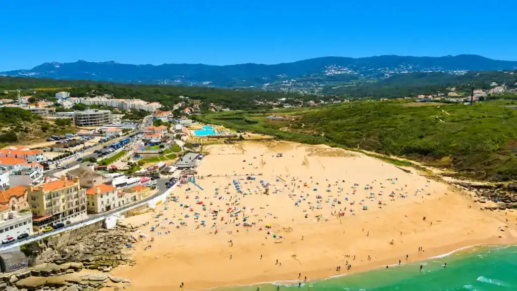 Praia das Maçãs wide sandy beach dotted with sunbathers and colourful umbrellas backed by the Sintra hills