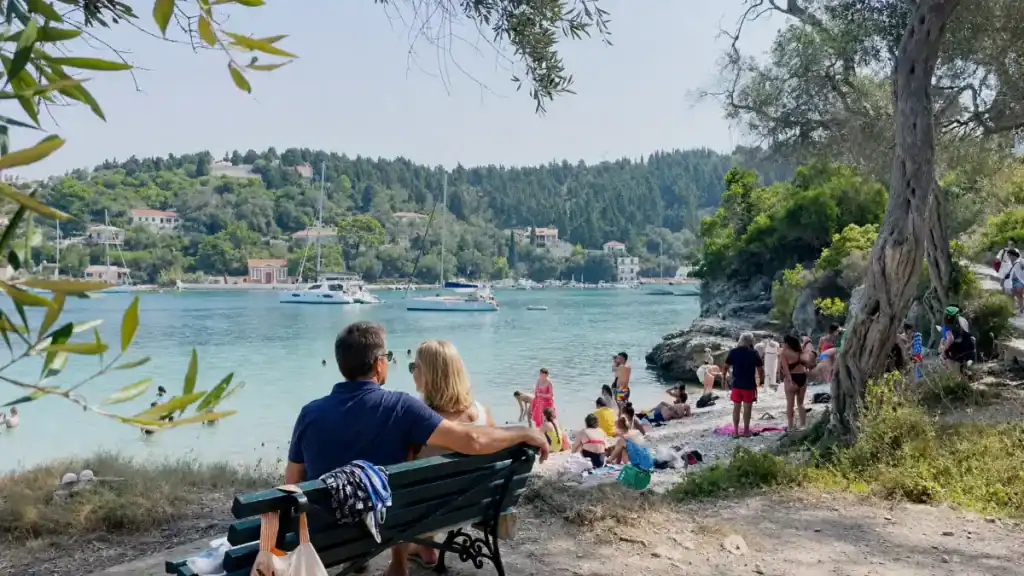 Couple on a bench overlooks Kanoni harbour, framed by olive trees near the best beaches in Paxos.