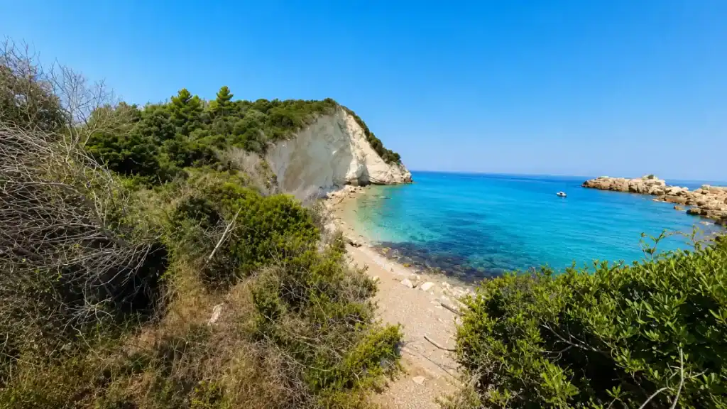 A dirt trail through scrub descends toward Komeno Beach's white cliffs and turquoise cove.