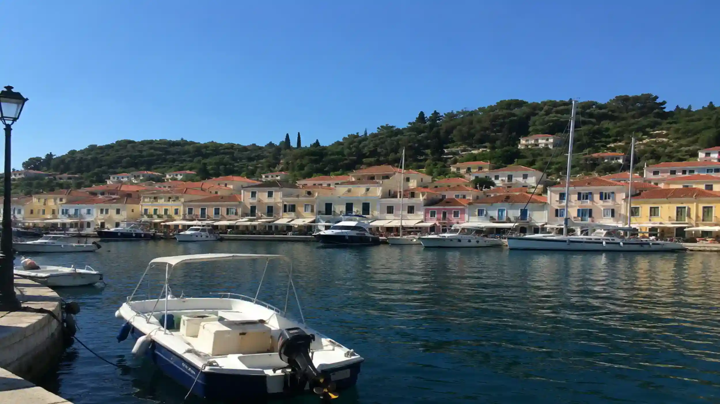 Moored boats along Gaios harbour with pastel houses under a wooded hillside, ideal for the best time to visit Paxos