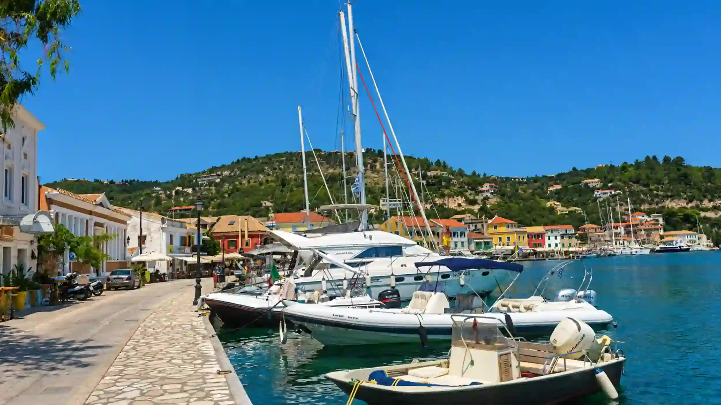 Motor boats and a yacht docked along the stone quay of Gaios with neoclassical buildings behind