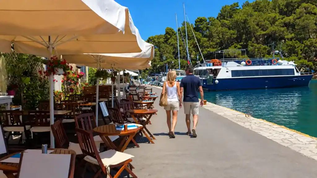 Walkers strolling past flower-draped restaurant terraces along the Gaios waterfront promenade