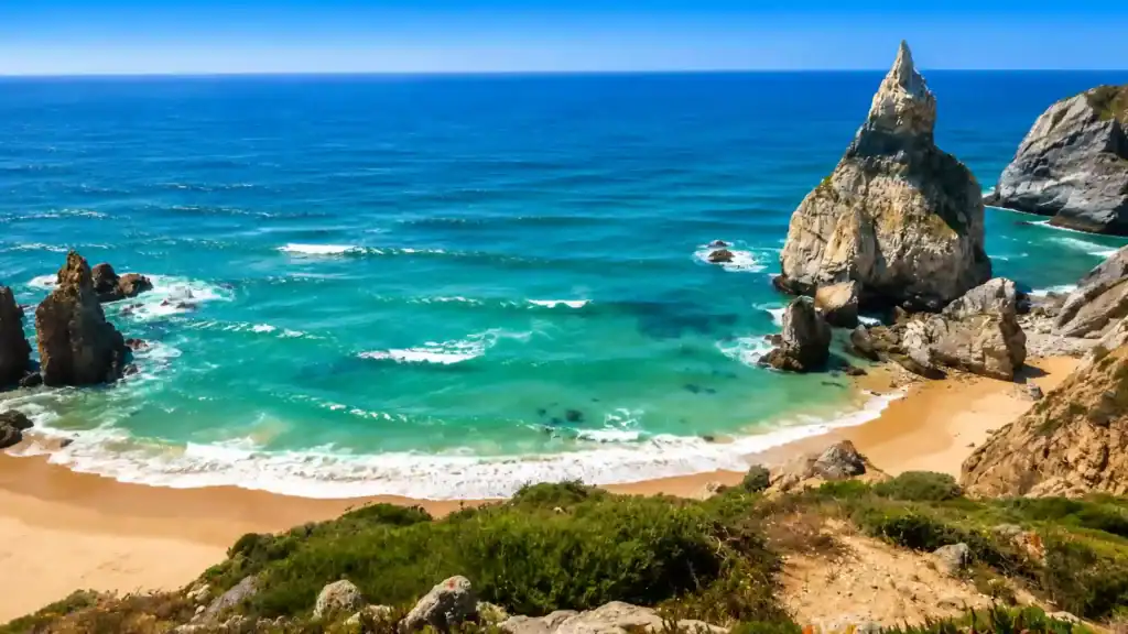 Jagged limestone sea stacks framing the sandy cove at Praia da Adraga, Colares