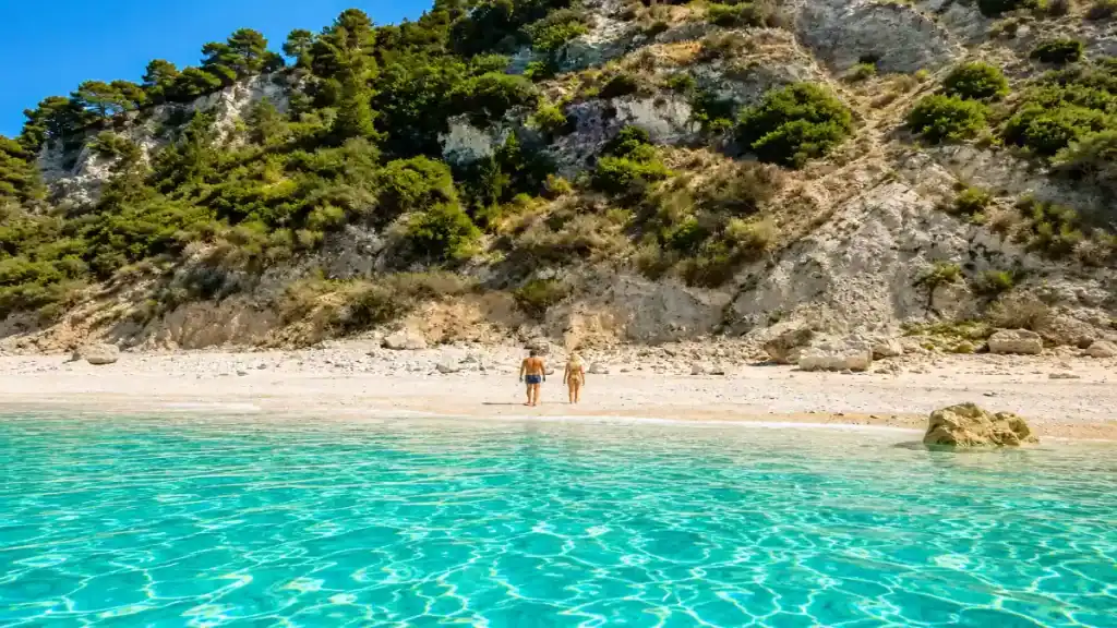 A couple walks along the pebbled shore of Voutoumi Beach.
