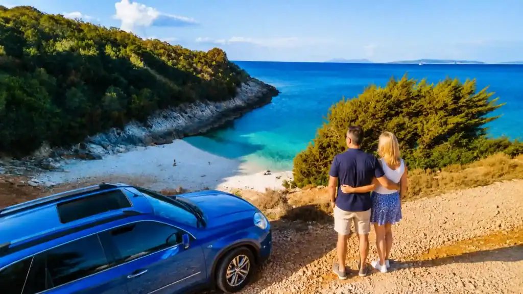 Couple parked above a secluded pebble cove, exploring whether you need a car in Paxos.