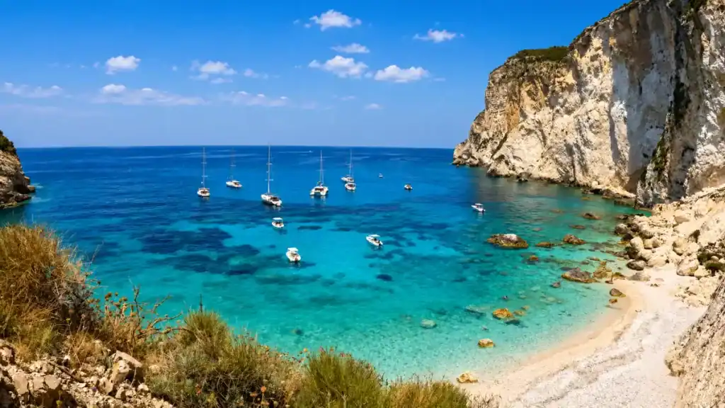 Sailboats anchored in the turquoise waters below towering cliffs at Erimitis.