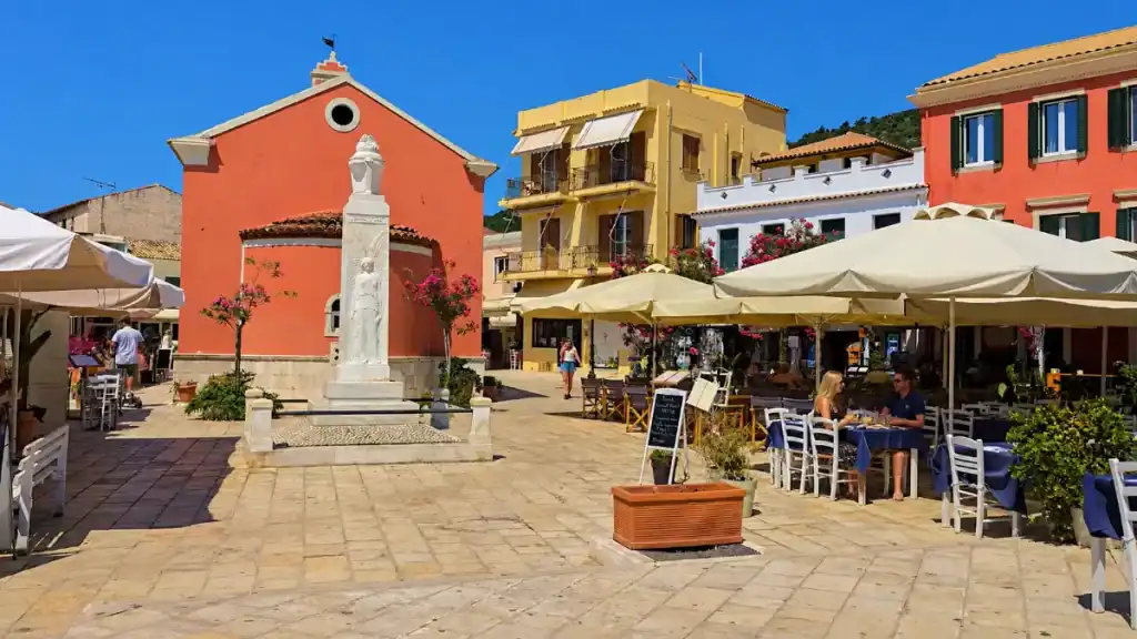 A marble memorial statue stands in Gaios square among terrace cafes and pastel buildings.