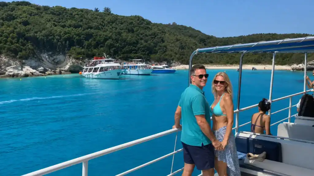 Couple on a boat deck overlooking Voutoumi Bay's turquoise water and anchored excursion boats.