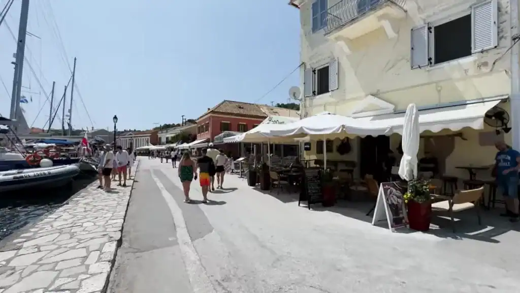 Pedestrians stroll the paved waterfront lined with cafรฉs and moored yachts at Gaios harbour.