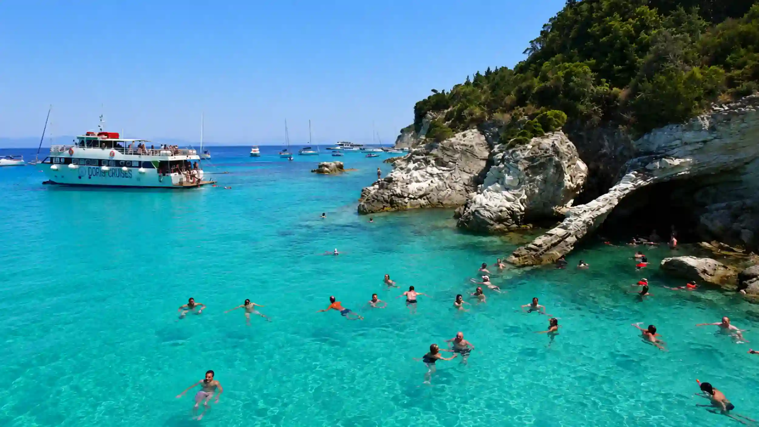 Swimmers in turquoise water near limestone rocks, is Antipaxos worth visiting for Voutoumi Beach.