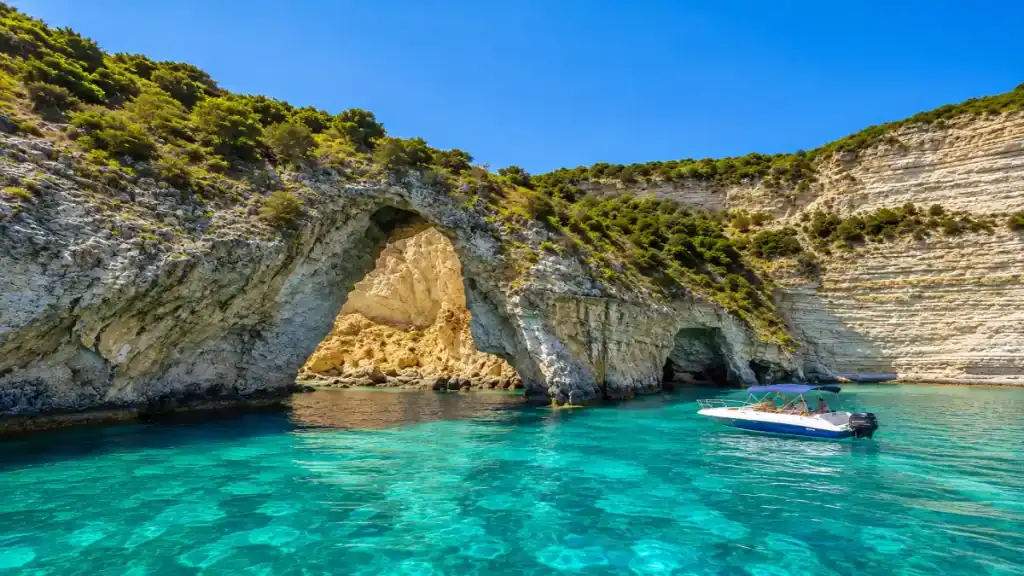A small motorboat drifts near a natural rock arch at Tripitos Arch, Antipaxos.