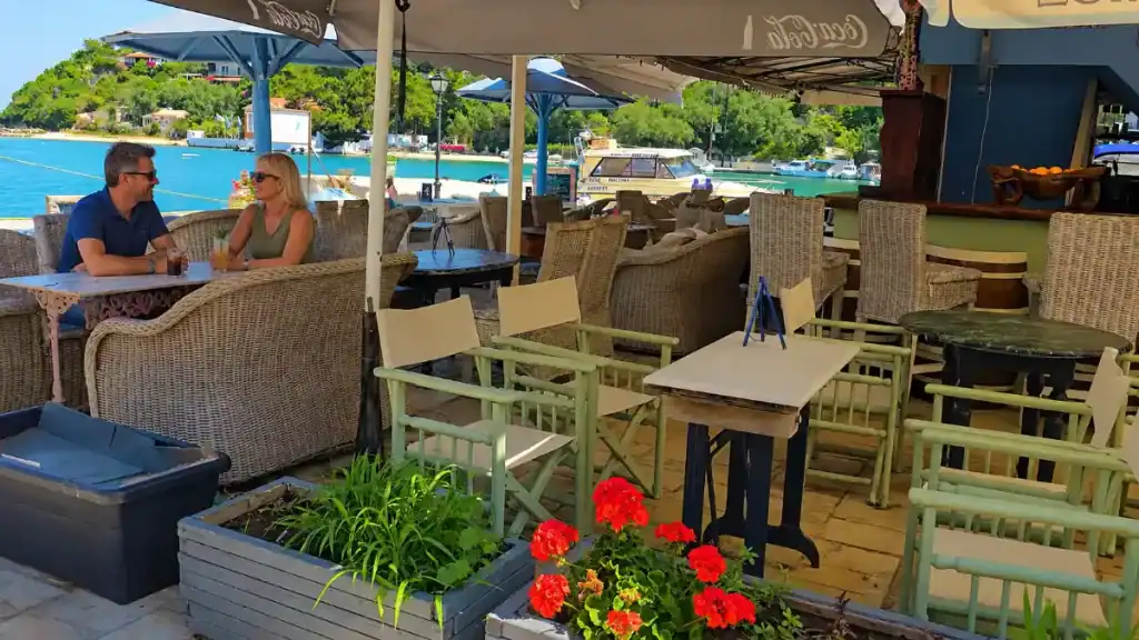 A couple shares drinks at a wicker table beside Lakka Bay