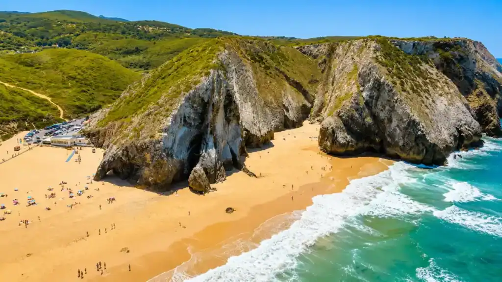 Dramatic rock formations dividing the golden sands of Praia da Adraga with turquoise Atlantic surf