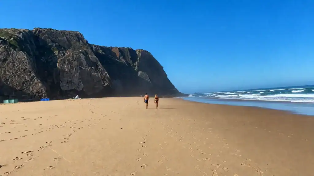 Couple walking along the wide sandy shore at Praia Grande Sintra