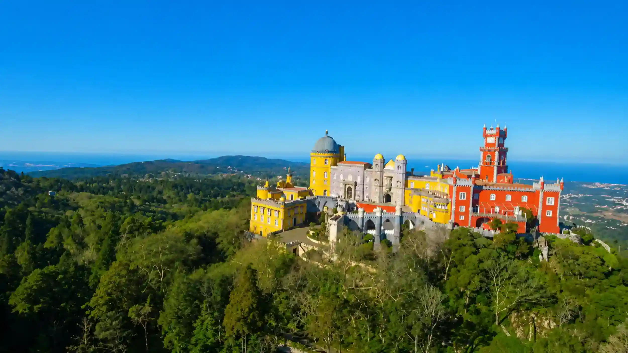 Yellow and red towers of Pena Palace crown a forested Sintra hilltop.