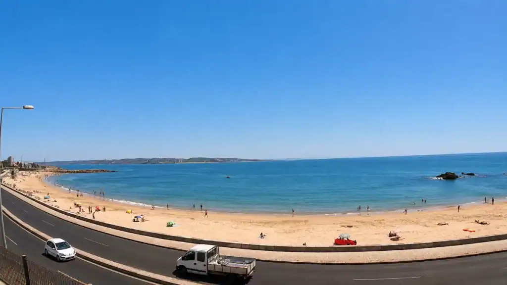 Sunbathers dot the curved sands of Praia da Ribeira beside the coastal road into Cascais.