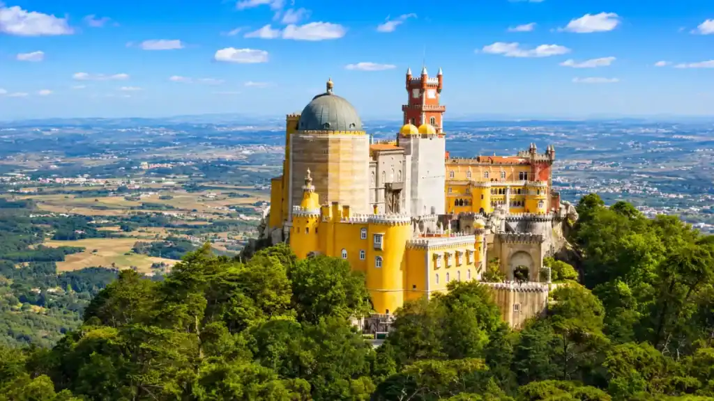 Yellow and red turrets of Pena Palace crown a forested hilltop above the Sintra valley.