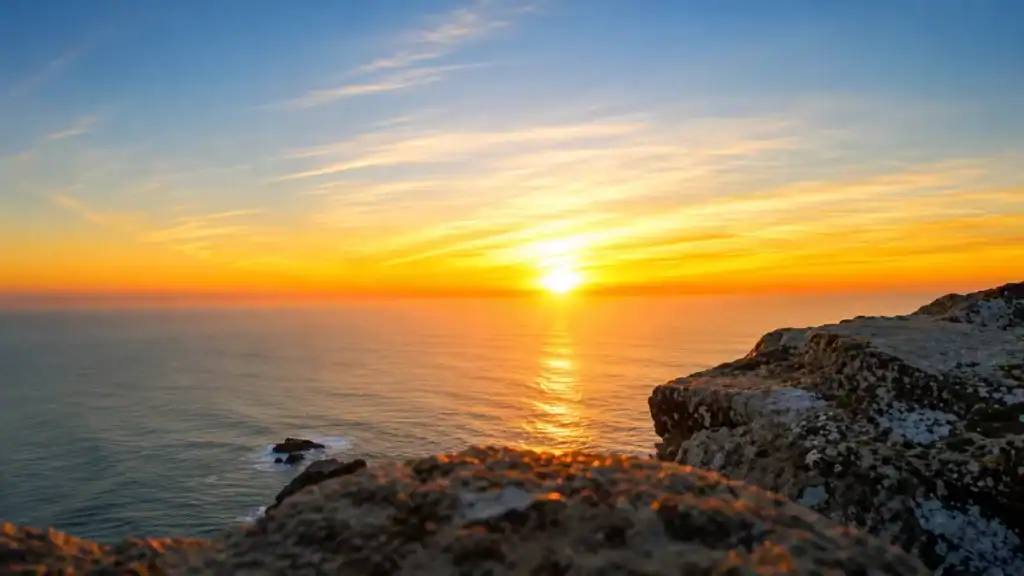 Lichen-covered rock frames an open Atlantic horizon as the sun sets directly ahead.