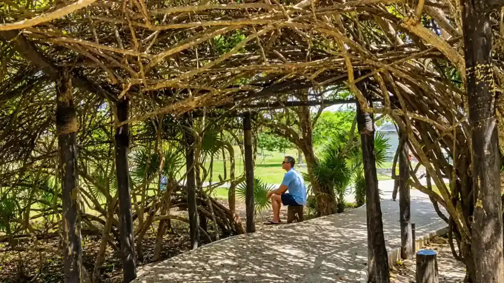 Visitor rests under a woven vine canopy on the path connecting the Tulum ruins to the coastal walkway