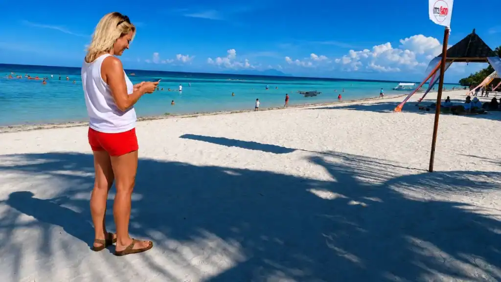 Woman checking her phone in the shade at Anda's white sand beach