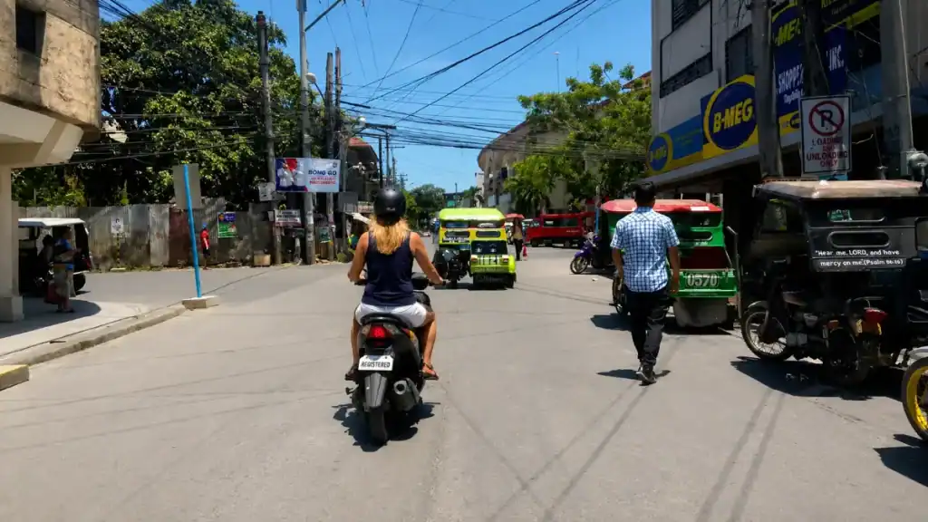 Woman riding a scooter past jeepneys and tricycles on a busy Tagbilaran street