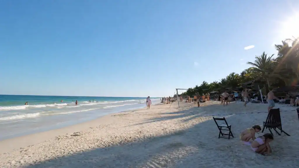 Sunbathers and swimmers along a white sand beach lined with palms in Tulum