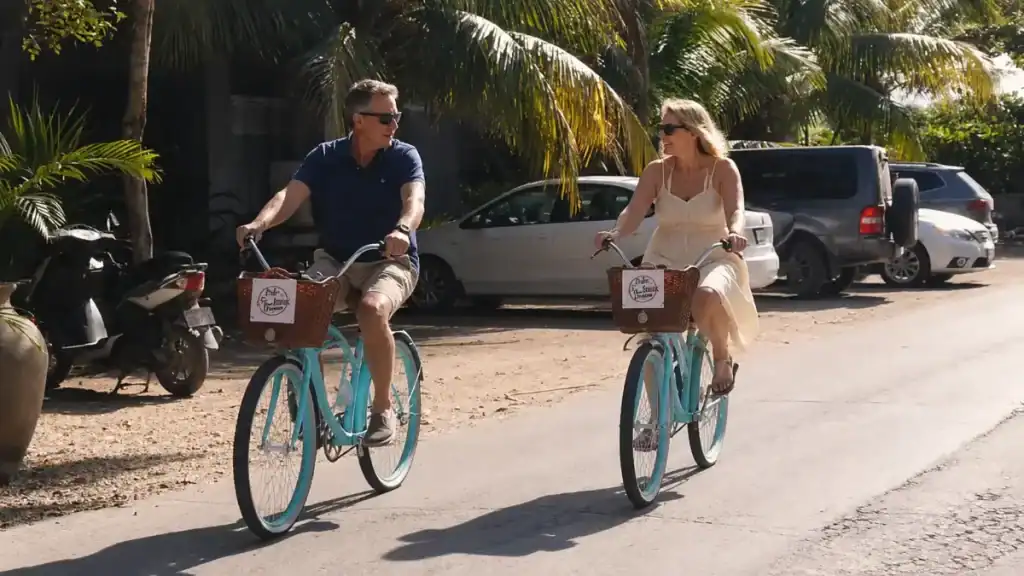 Couple riding turquoise beach cruisers past parked cars in Tulum, showing you don't always need a car in Tulum