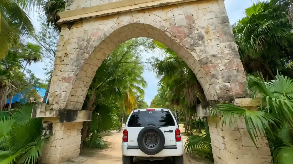 White Jeep passing under a stone archway on a jungle road in Tulum, showing why you need a car in Tulum