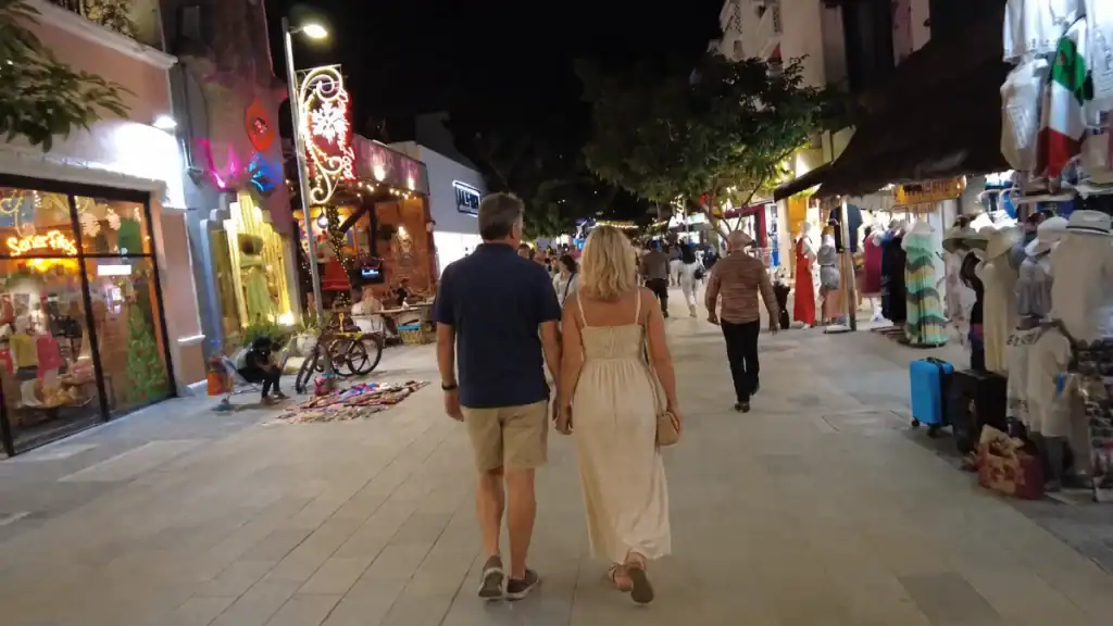 Couple holding hands strolling Tulum's pedestrian shopping street at night, no car needed here