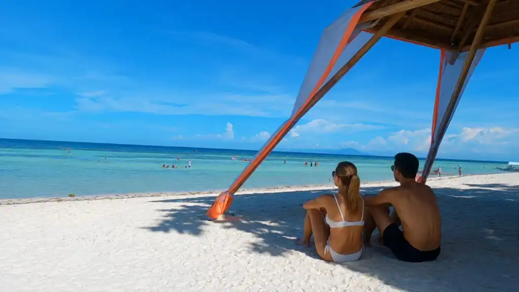 Couple relaxes under a bamboo shade hut on the white sand of Anda Beach