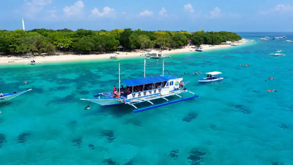 Outrigger boat anchors in turquoise water off Balicasag Island's coral shoreline