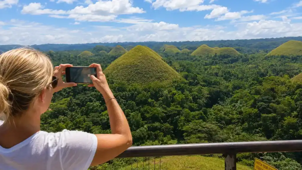 A traveler photographs the grass-covered mounds of Chocolate Hills from the Carmen viewpoint.