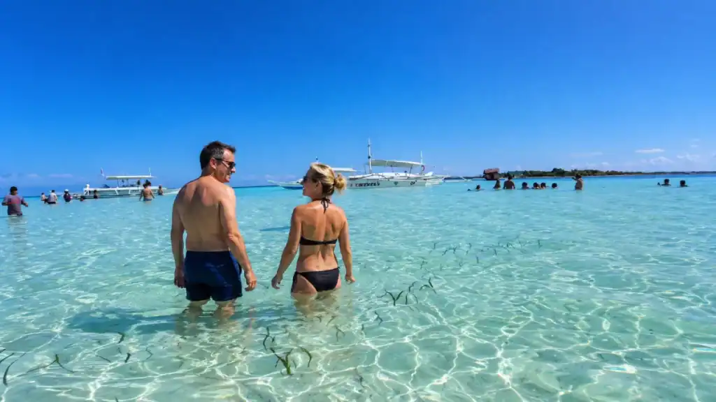 A couple wading through Balicasag Island's clear shallows shows why is Balicasag worth visiting for swimmers.