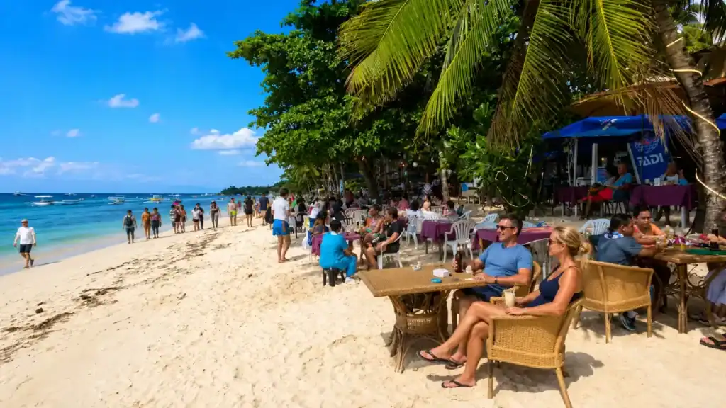 Beachfront cafe tables under palms line Panglao Beach, offering another reason is Balicasag worth visiting nearby.