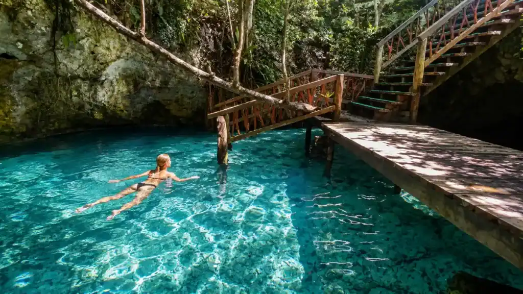Swimmer glides past a wooden platform beside Gran Cenote's stairway entrance.
