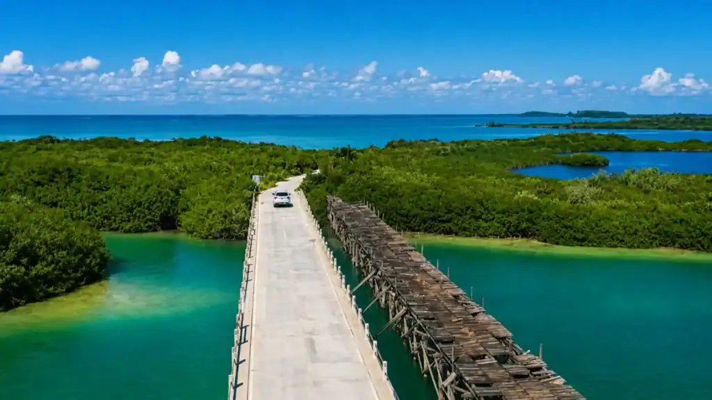 A car crosses a weathered wooden causeway between turquoise lagoons in Sian Ka'an.