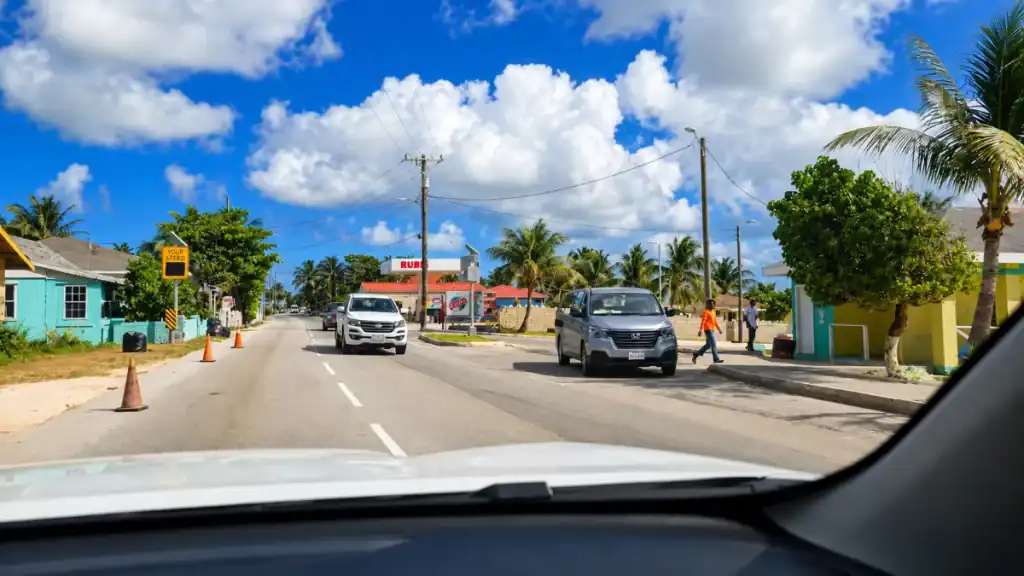 Traffic passes shops and palms on a residential Nassau street near a gas station.