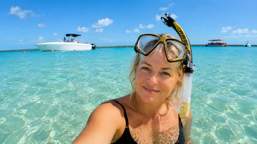 Snorkeler smiles beside a boat in the clear turquoise waters off Nassau, worth visiting for its reef trips