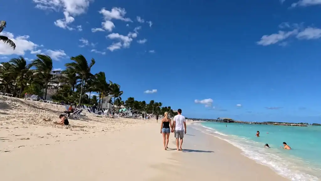A couple walks hand in hand along the shoreline at Cable Beach with palm trees framing the sand.