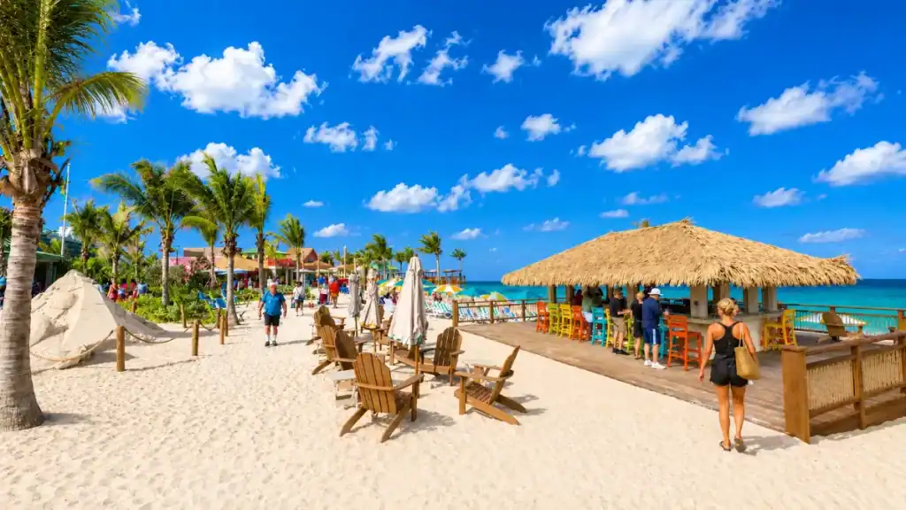 Wooden beach chairs sit near a thatched-roof bar on Paradise Island's sandy shoreline.
