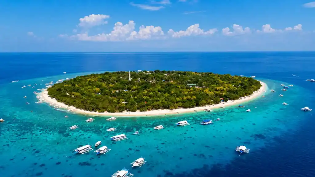 Outrigger boats anchor in turquoise reef shallows ringing Balicasag Island.