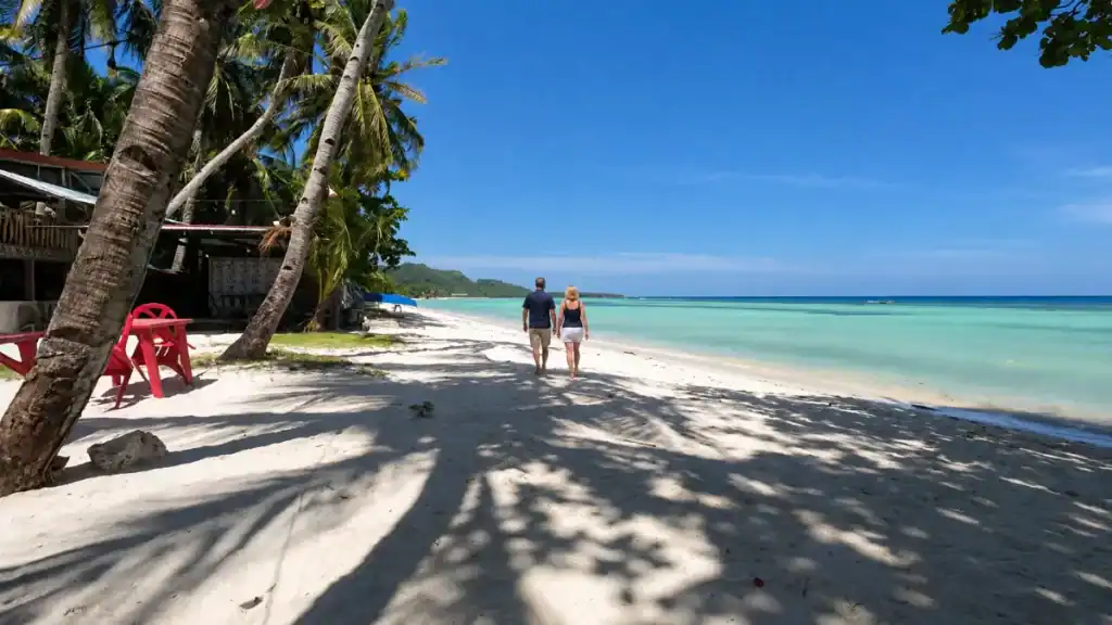 A couple strolls the palm-shaded shoreline of Quinale Beach, Anda's quiet answer in the Panglao vs Anda debate.