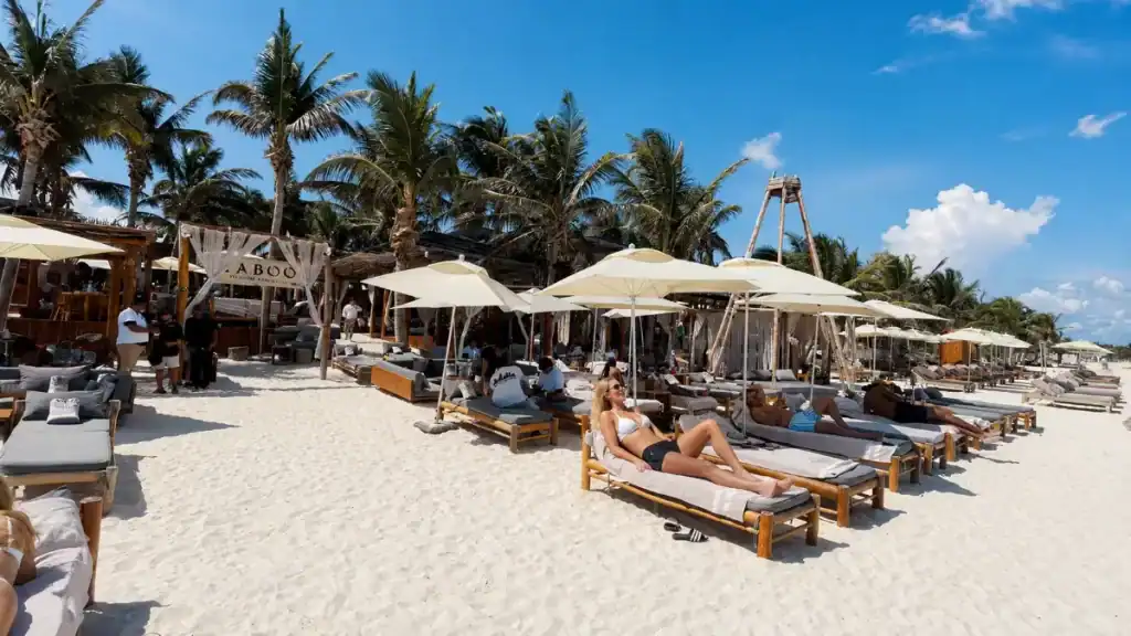 Sunbathers on wooden loungers under umbrellas at a Tulum beach club, revealing what is Tulum really like