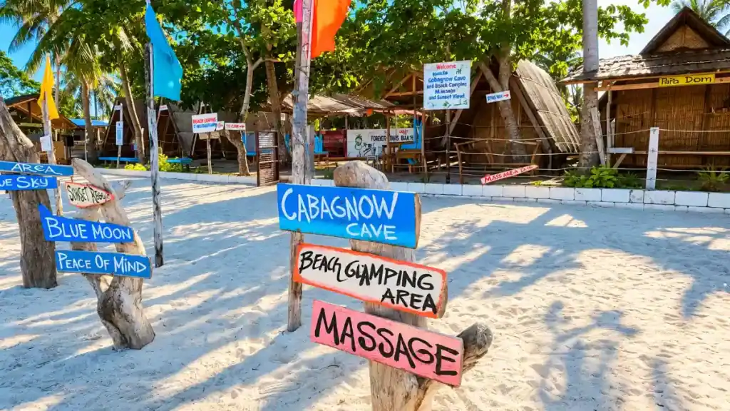 Weathered driftwood signs mark glamping huts and a nearby cave on an Anda beach