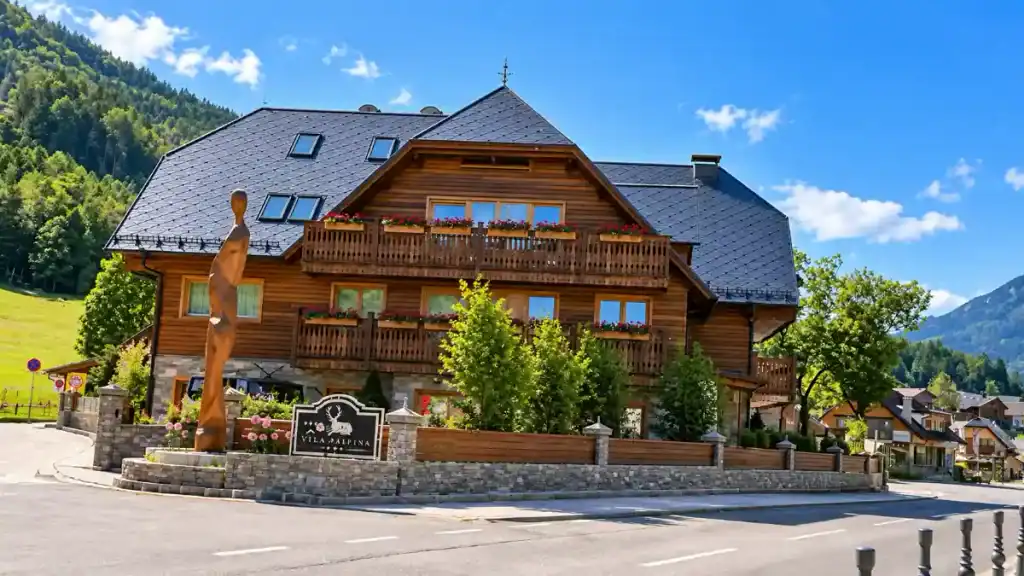 Timber chalet with flower-lined balconies and stag emblem sign on roadside corner