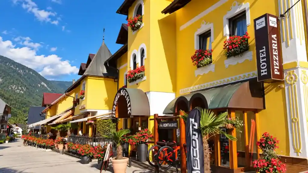 Yellow hotel facade decked in red geraniums with a bike rental stand out front.