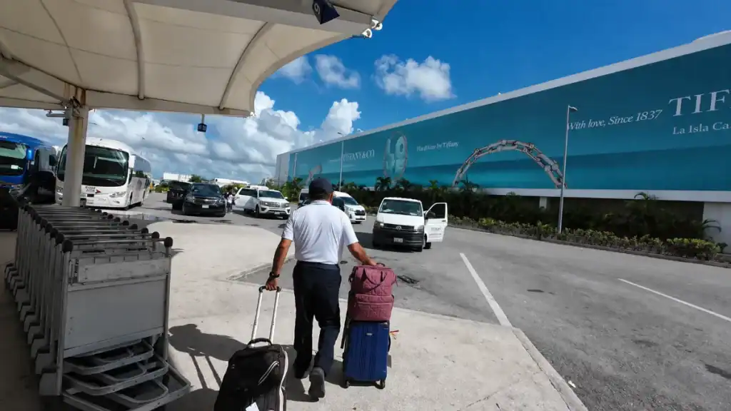 Porter wheeling luggage toward transfer vans outside Cancún airport, the first step for how to get to Holbox