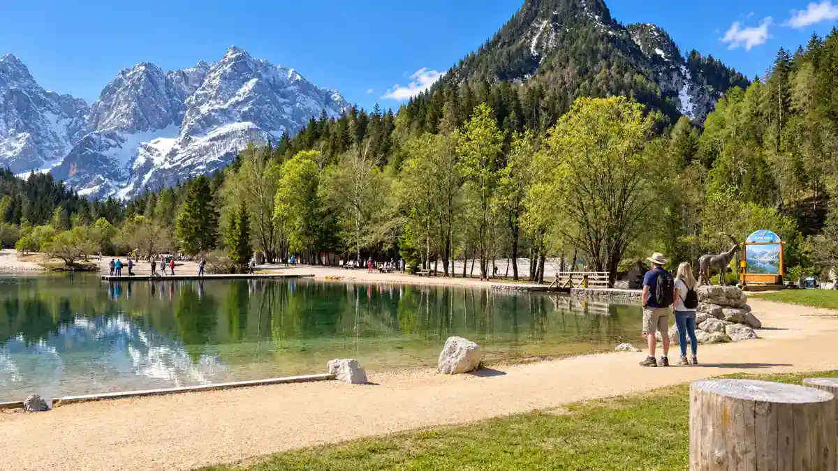 Walkers pass an ibex statue on the shore path at Lake Jasna, one reason many wonder do you need a car in Kranjska Gora when the lake sits so close to town